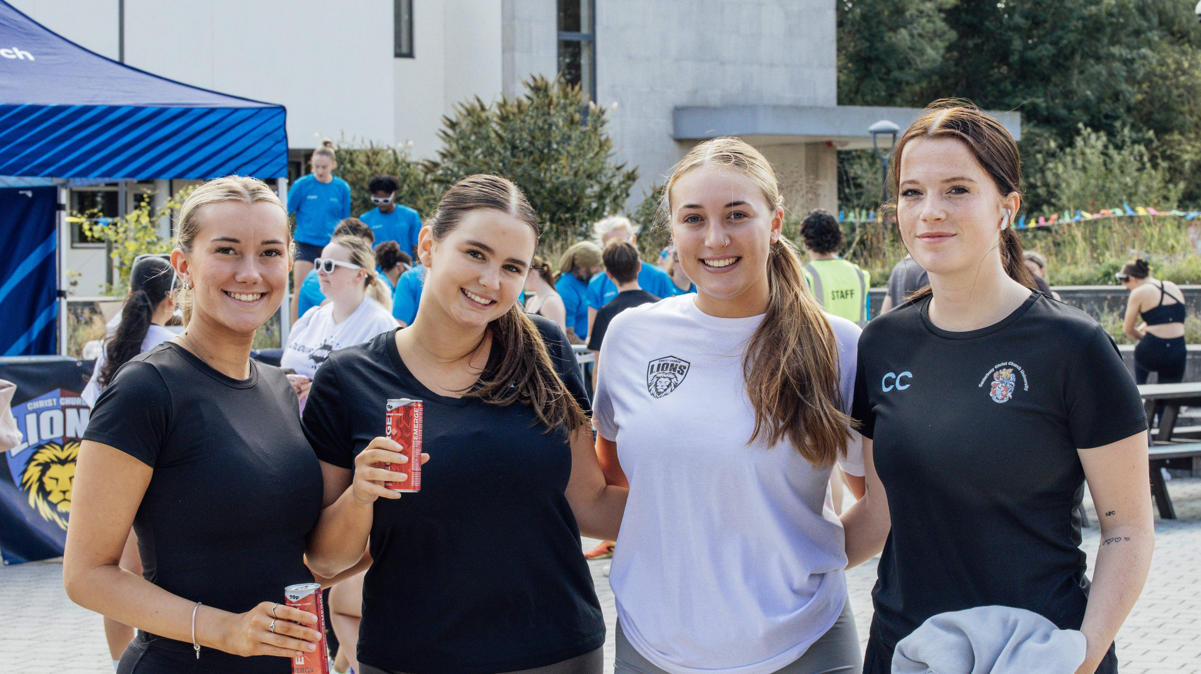 A group of 4 students smiling at the camera with an event taking place behind them.